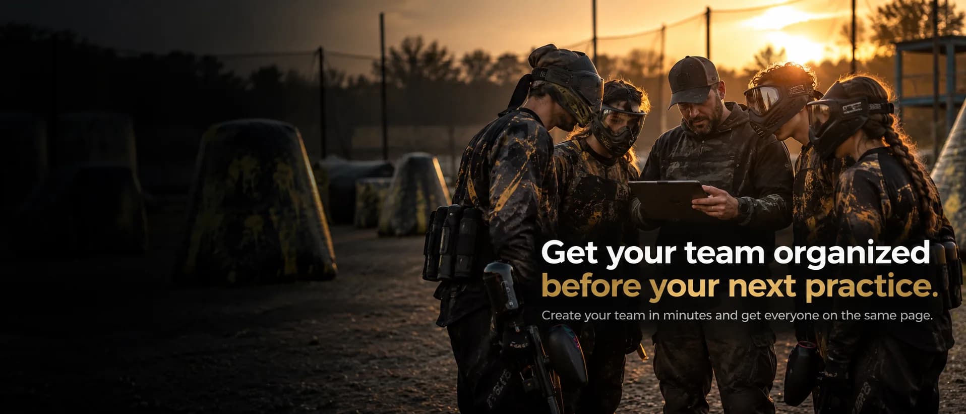 A coach showing a tablet to his masked players on a paintball field at sunset